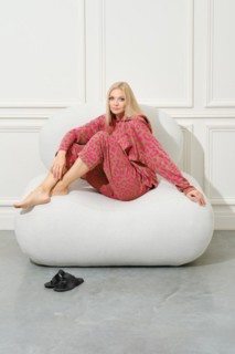 Barefoot woman in pink pyjama sitting on couch in a bright room