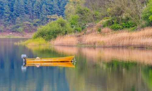 Small yellow metal fishing boat with small engine mount floating peacefully on a lake in South