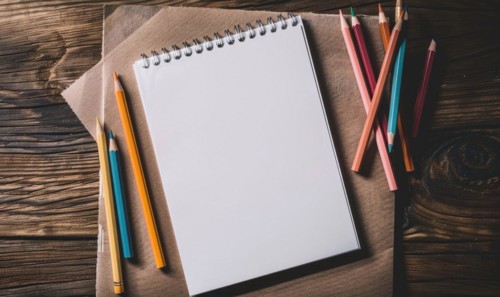 A sketchbook open to a blank page with graphite pencils beside it AI generated