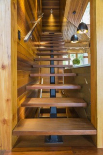 Looking up illuminated wooden staircase with opened steps and clear glass railing leading to