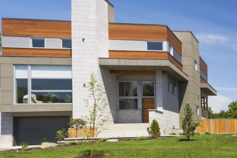 Two story grey and charcoal stone with cedar wood siding modern cube style home facade in summer,