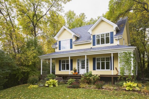 Two storey yellow clapboard with blue and white trim cottage style home facade in autumn, Quebec,