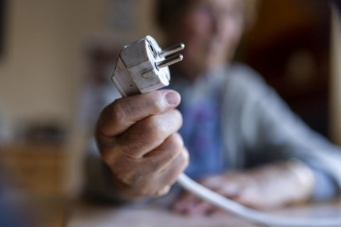 Senior citizen holding a power cable with plug in her hand at home, symbolising energy costs and