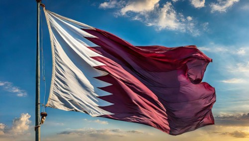 The flag of Qatar flutters in the wind, isolated against a blue sky