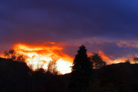 Sunset with dramitic dark clouds, sun shining through a gap in the clouds, red sky, burning sky,