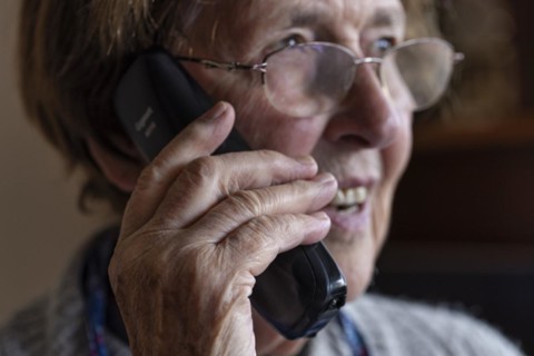 Laughing senior citizen with smock talking on the phone at home in her living room, Cologne, North