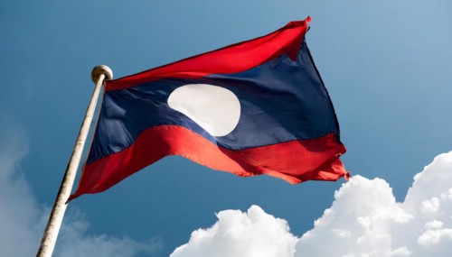 The flag of Laos flutters in the wind, isolated against a blue sky