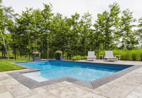 Two white long chairs on edge of in-ground swimming pool with flowers in planters in residential