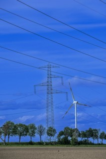 Electricity pylon with high-voltage lines and wind turbine on the K63 road with trees at the Avacon