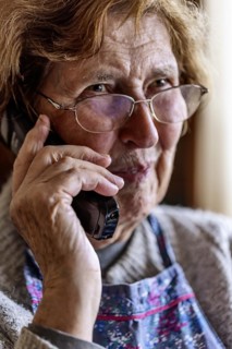 Laughing senior citizen with smock talking on the phone at home in her living room, Cologne, North