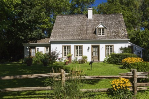 Old circa 1886 white with beige and brown trim Canadiana cottage style home facade with landscaped