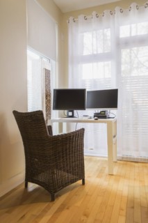 Brown high-back wicker chair and white desk table with computer in home office in master bedroom