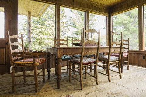 Sun room with antique wooden harvest dining table and chairs, treated wood floorboards inside a
