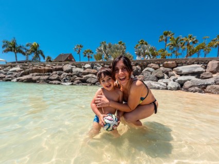 A woman and a child are playing in the water. The woman is holding a ball and smiling. Scene is