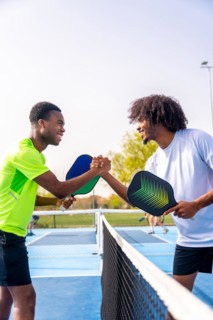 Vertical side view of two african sportive men shaking hands before playing pickleball