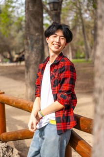 Vertical portrait of an asian gay man standing in a park smiling at camera