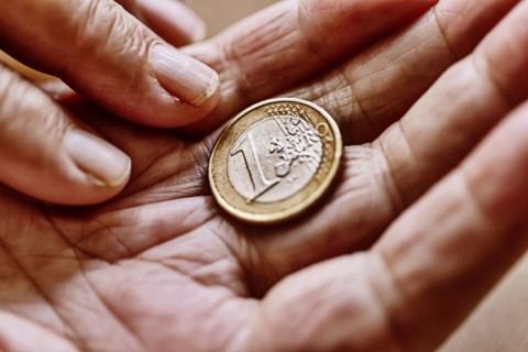 A euro coin in the wrinkled hand of a senior citizen, symbolising poverty and poverty in old age
