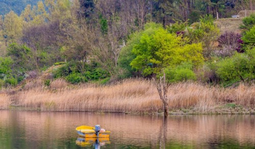 Small yellow metal fishing boat with small engine mount floating peacefully on a lake in South