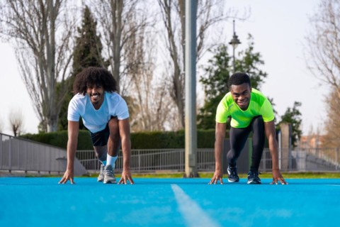Frontal view of two sportive young african males in position to start a race in a blue running