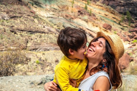 A woman and a child are hugging in a field. The woman is wearing a straw hat. Scene is warm and
