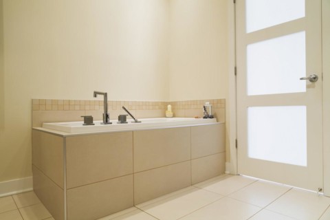 Soaking tub encased in a ceramic tile base in bathroom inside a renovated ground floor apartment in