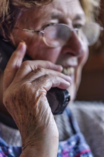 Laughing senior citizen with smock talking on the phone at home in her living room, Cologne, North
