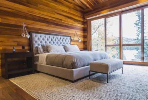 King size bed with grey upholstered panel headboard, ottoman and wooden end tables in master