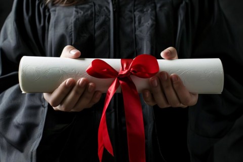 Degree paper certificate roll with red ribbon held by young woman in graduation robe. KI generiert,