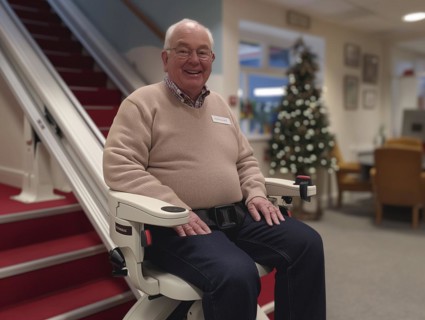 A pensioner rides a stair lift up a flight of stairs, AI generated
