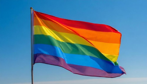 The rainbow flag flutters in the wind, isolated, against the blue sky. In many cultures around the