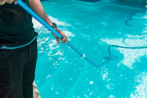 Person cleaning a swimming pool with a vacuum hose. Man cleaning swimming pool with suction hose