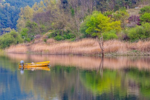 Small yellow metal fishing boat with small engine mount floating peacefully on a lake in South