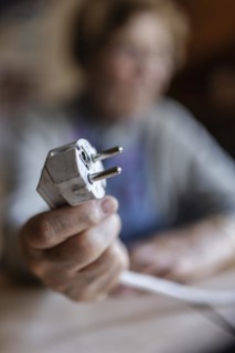 Senior citizen holding a power cable with plug in her hand at home, symbolising energy costs and