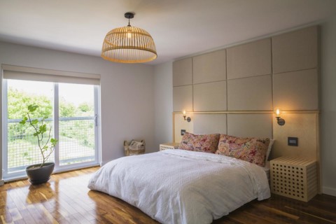 King size bed covered with white bedspread in bedroom with American walnut hardwood flooring on