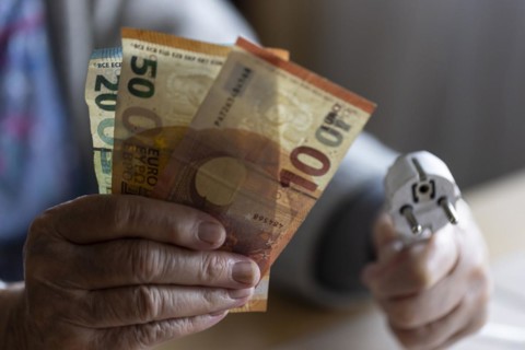 Senior citizen holding money and a power cable with plug in her hand at home, symbolising energy