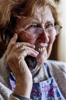 Laughing senior citizen with smock talking on the phone at home in her living room, Cologne, North
