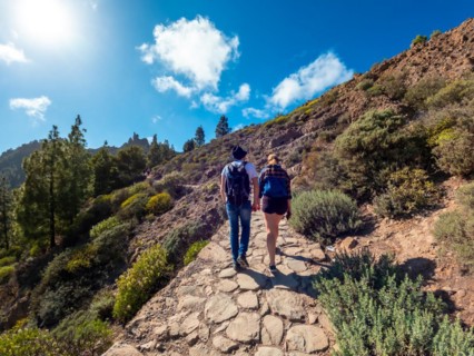 A man and woman are walking on a path in the woods. The woman is wearing a backpack and the man is
