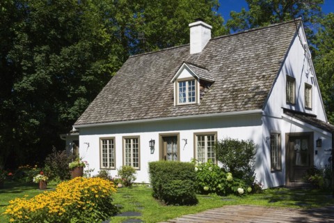 Old circa 1886 white with beige and brown trim Canadiana cottage style home facade with landscaped