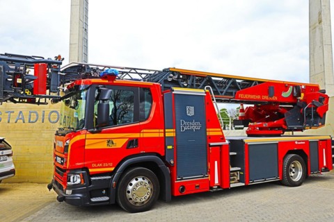 A red fire engine with a turntable ladder is parked in front of a stadium