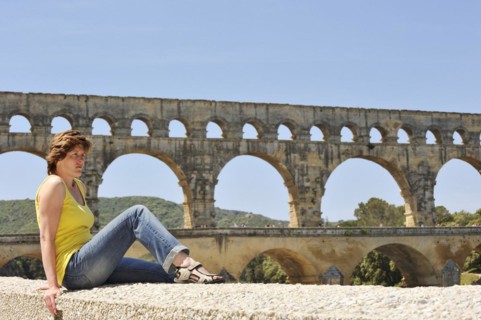 Woman sitting on a wall in front of the Pont du Gard, Roman aqueduct over the river Gardon,