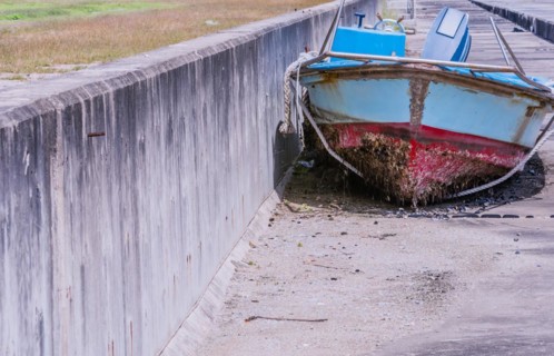 Front view of old dilapidated red, white and blue fishing boat with barnacles on bottom sitting on