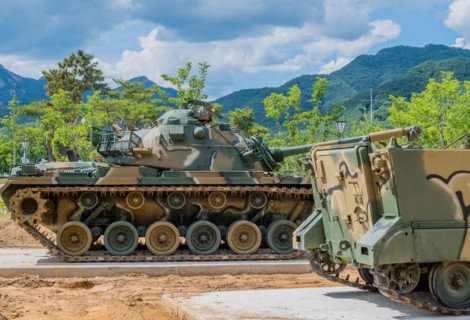 Side view of camouflaged tank used in Korean war behind armored landing vehicle on display in