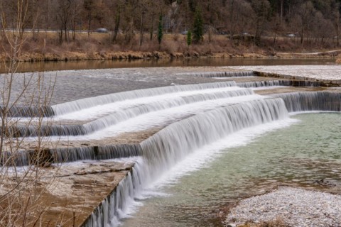 Stepped waterfall flows into a calm river in a wooded landscape, Bad Reichenhall, Bavaria, Germany,