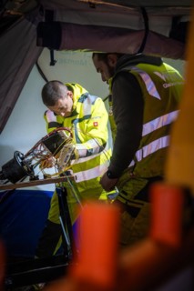 Worker carrying out electrical installation work in an illuminated work tent during the night,
