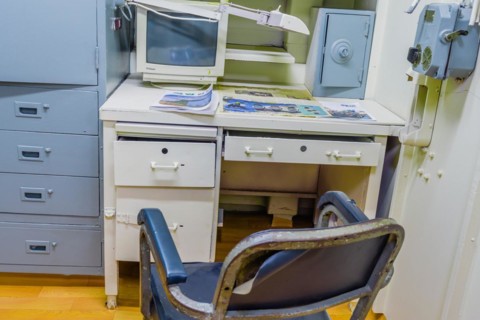 Interior of officer's cabin with desk chair computer and magazines inside battleship on display at