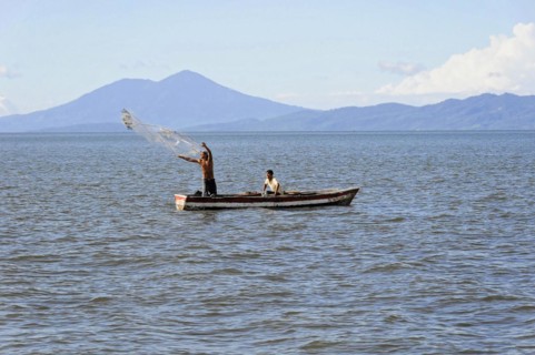 Lake Nicaragua, Two men in a boat casting a fishing net on a lake, mountains in the background,