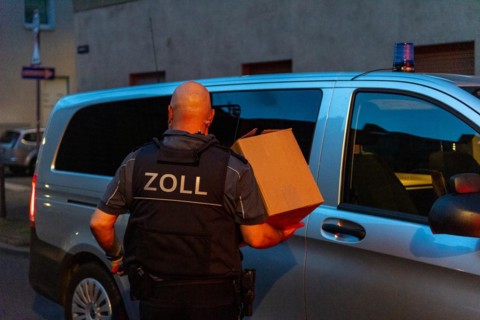 A customs officer carries a cardboard box to an official vehicle in the evening, The Cologne police