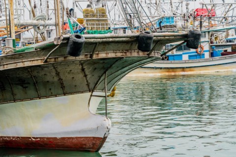 Closeup of bow of large fishing vessel anchored in harbor with other boats and rigging in the