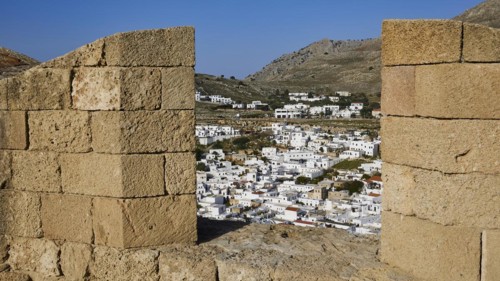 View through an old stone wall to a settlement with white houses and mountains in the background,