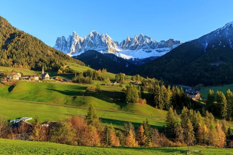Sunlit village in a valley below a snow-covered mountain range, Italy, Trentino-Alto Adige, Alto